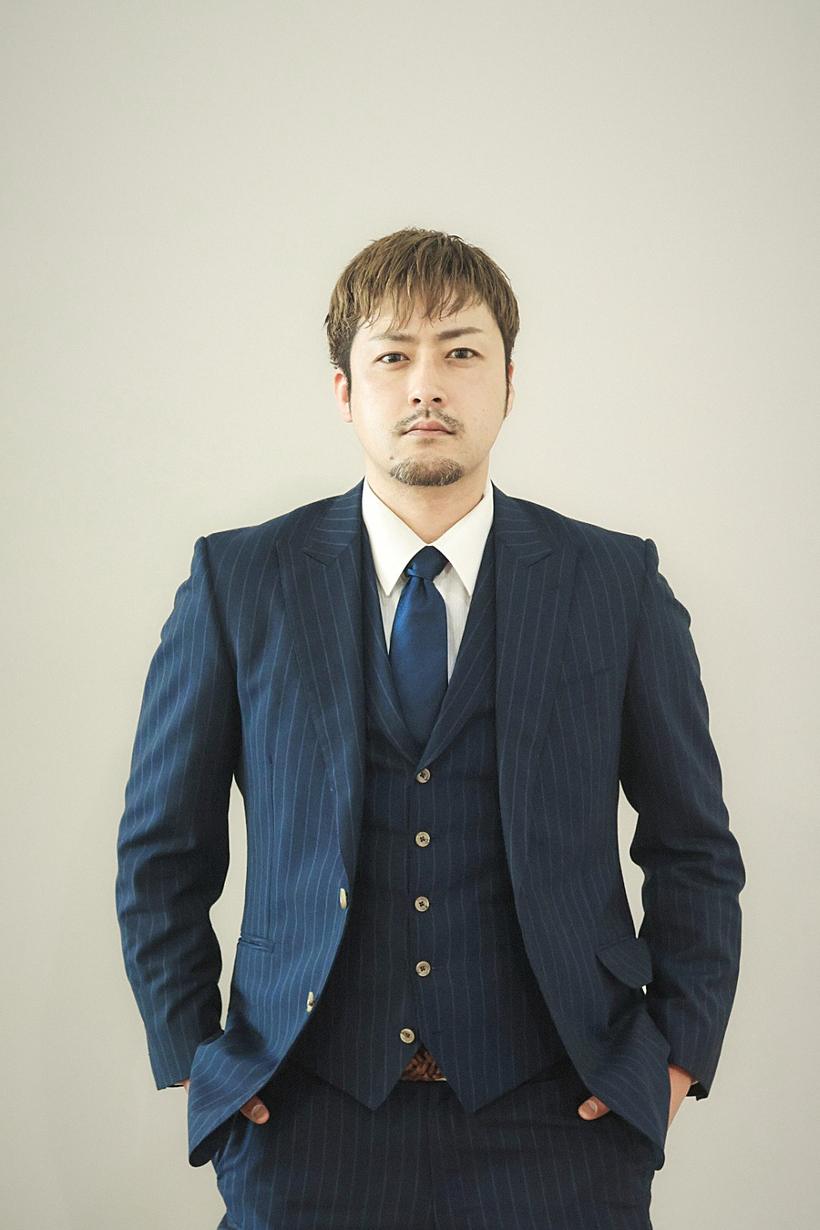 白背景スタジオで正面に立つ、ネイビーストライプの三つ揃えスーツの男性